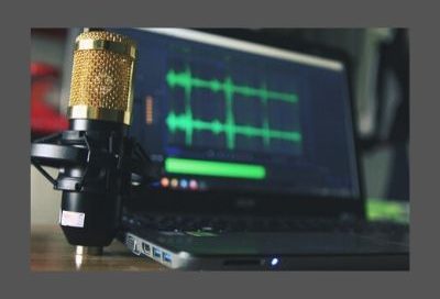 Image shows a microphone beside a laptop computer with green audio waves displayed on the screen