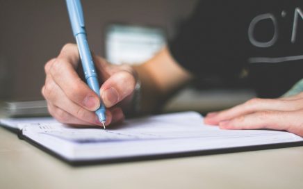 Image shows a woman writing in a notebook with a blue pen