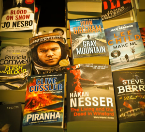 Image shows books stacked on a table in a bookshop including Lee Child, John Grisham, Steve Berry and Patricia Cornwell