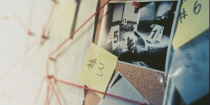 A detective's investigation board covered with photos, yellow post it notes and red string connecting the clues together